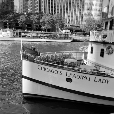 Black and white photo of Chicago's Leading Lady boat with a She Builds® flag on the bow of the boat.